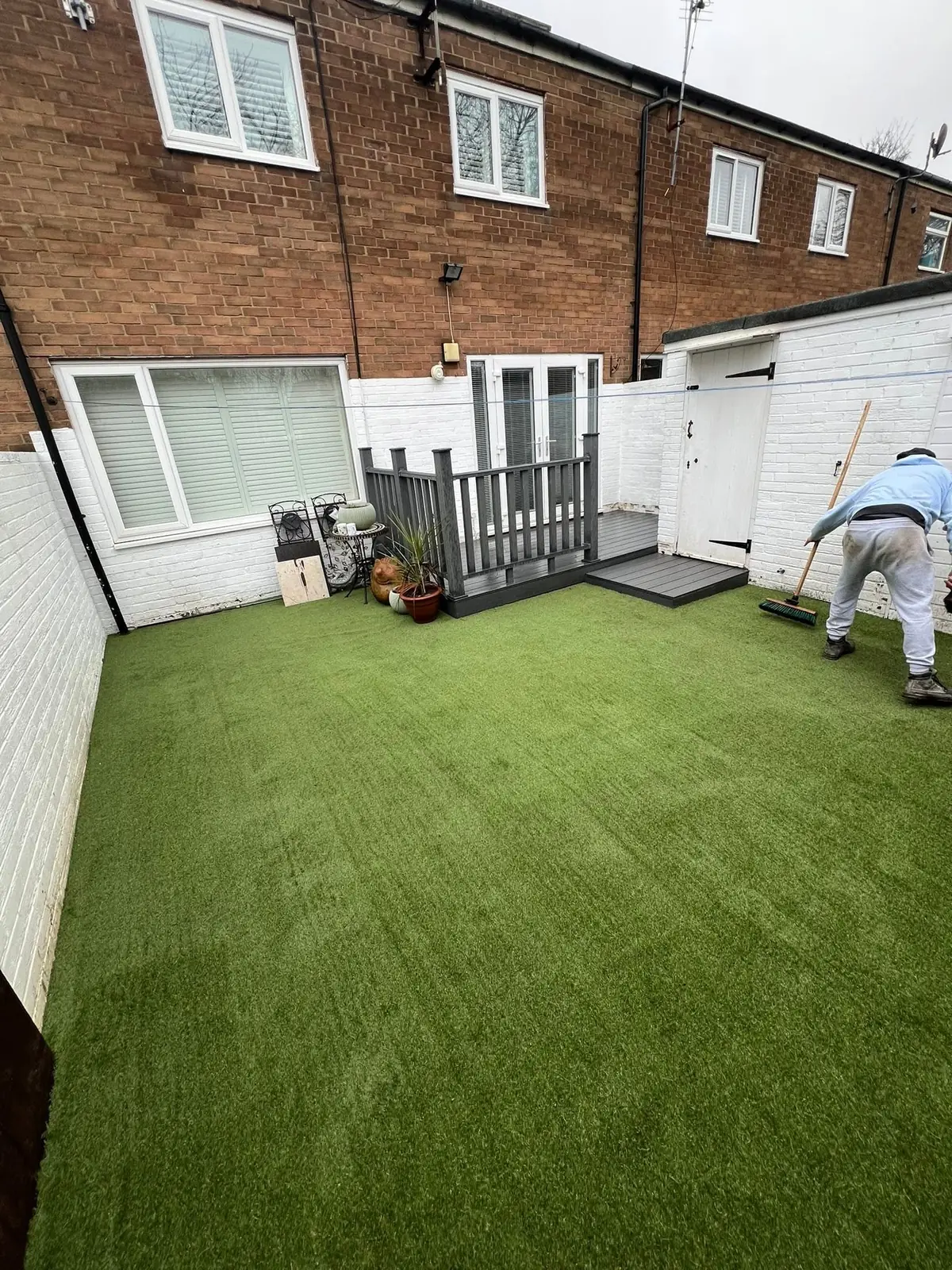 Artificial grass being laid and brushed out in the finished garden