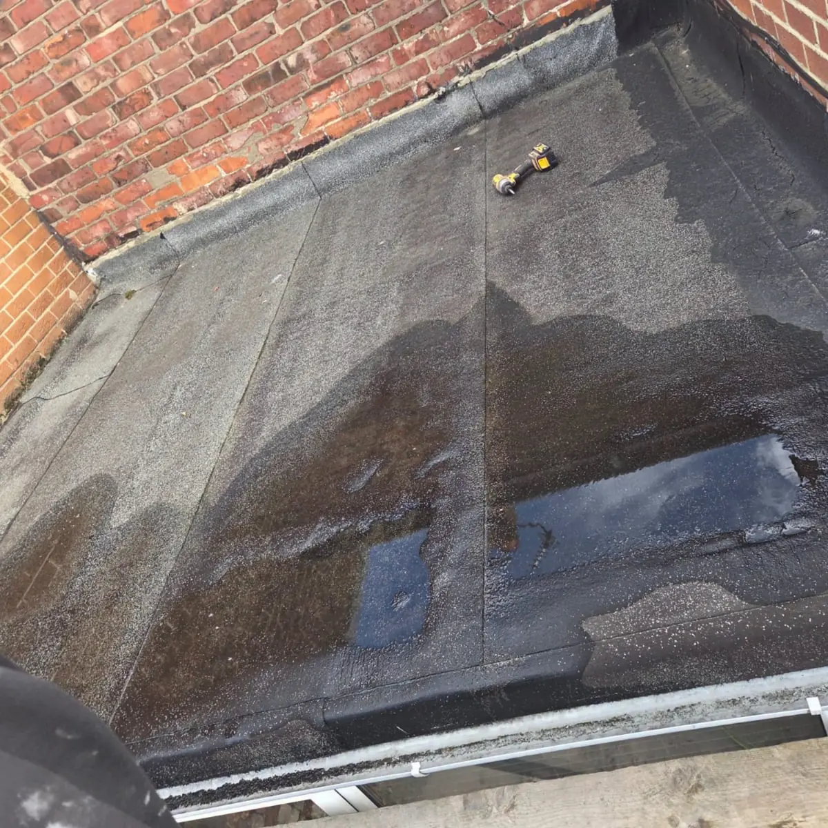 An old felt flat roof with standing water pooled across the surface