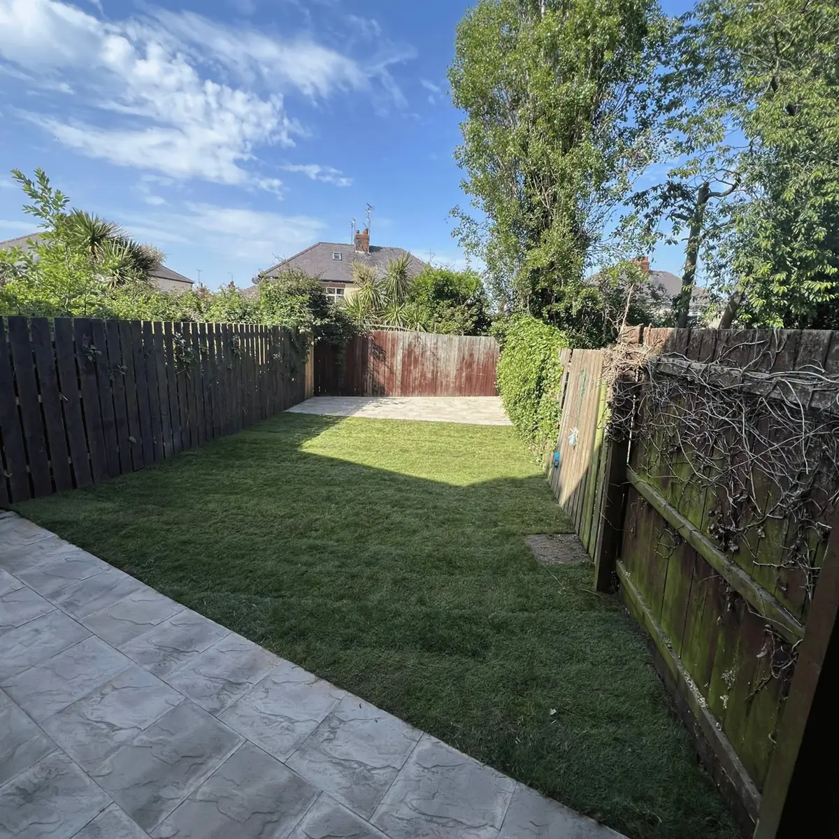 The same garden after clearing, with fresh turf laid and a patio at the far end